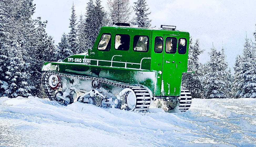 Green snow vehicle driving away on snowy mountaintop