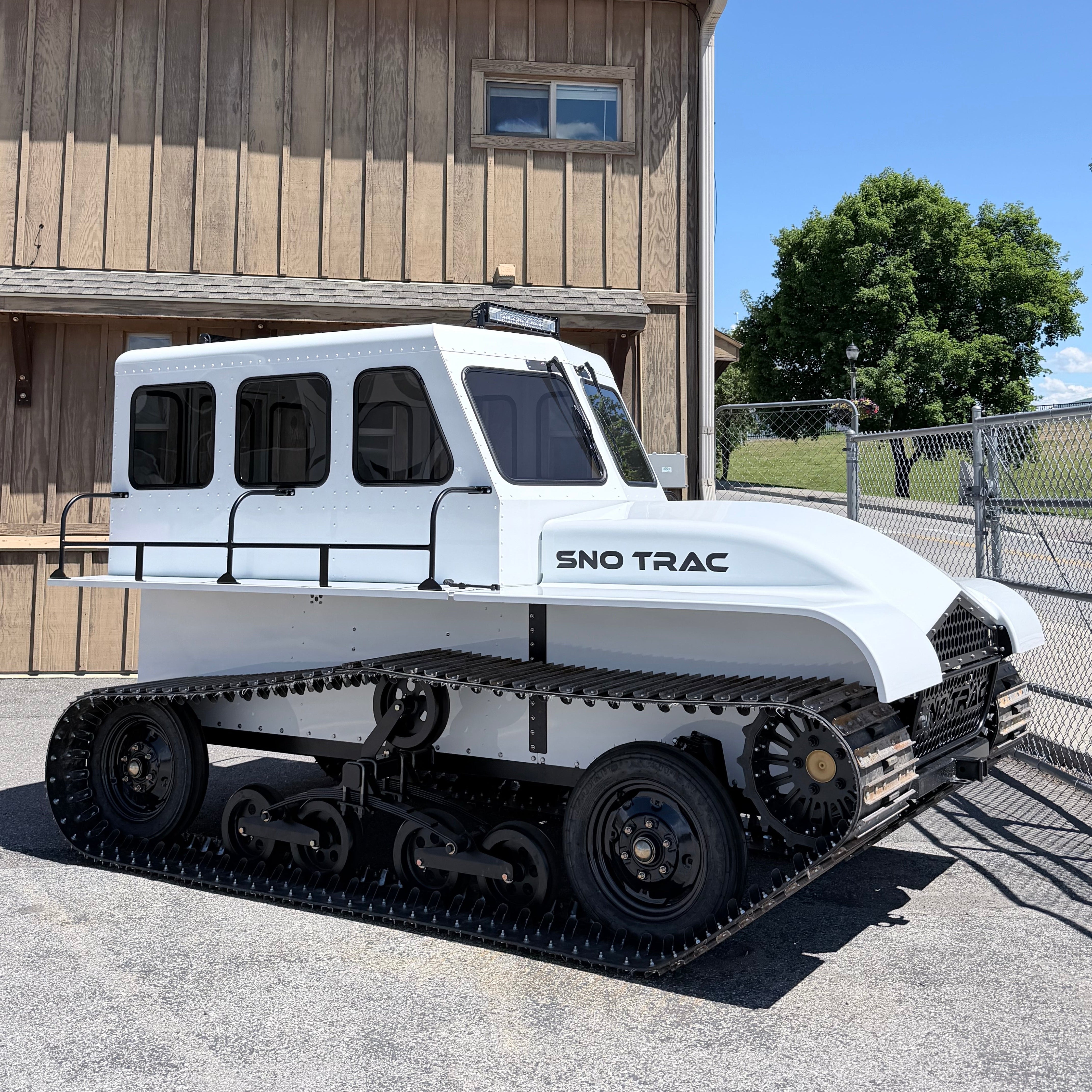 White Sno Trac vehicle parked in front of a wooden building with a clear blue sky.