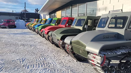 Row of colorful snowmobiles parked in a snowy area with a building in the background.