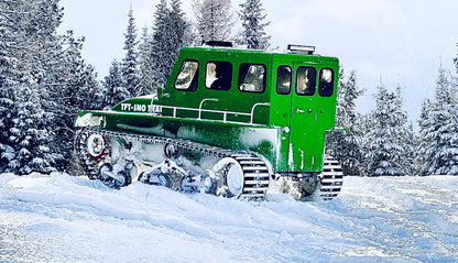 Green snow vehicle driving away on snowy mountaintop