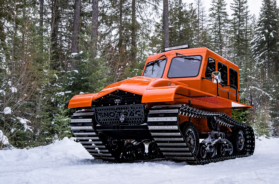 Orange Sno Trac vehicle on snowy mountain top.