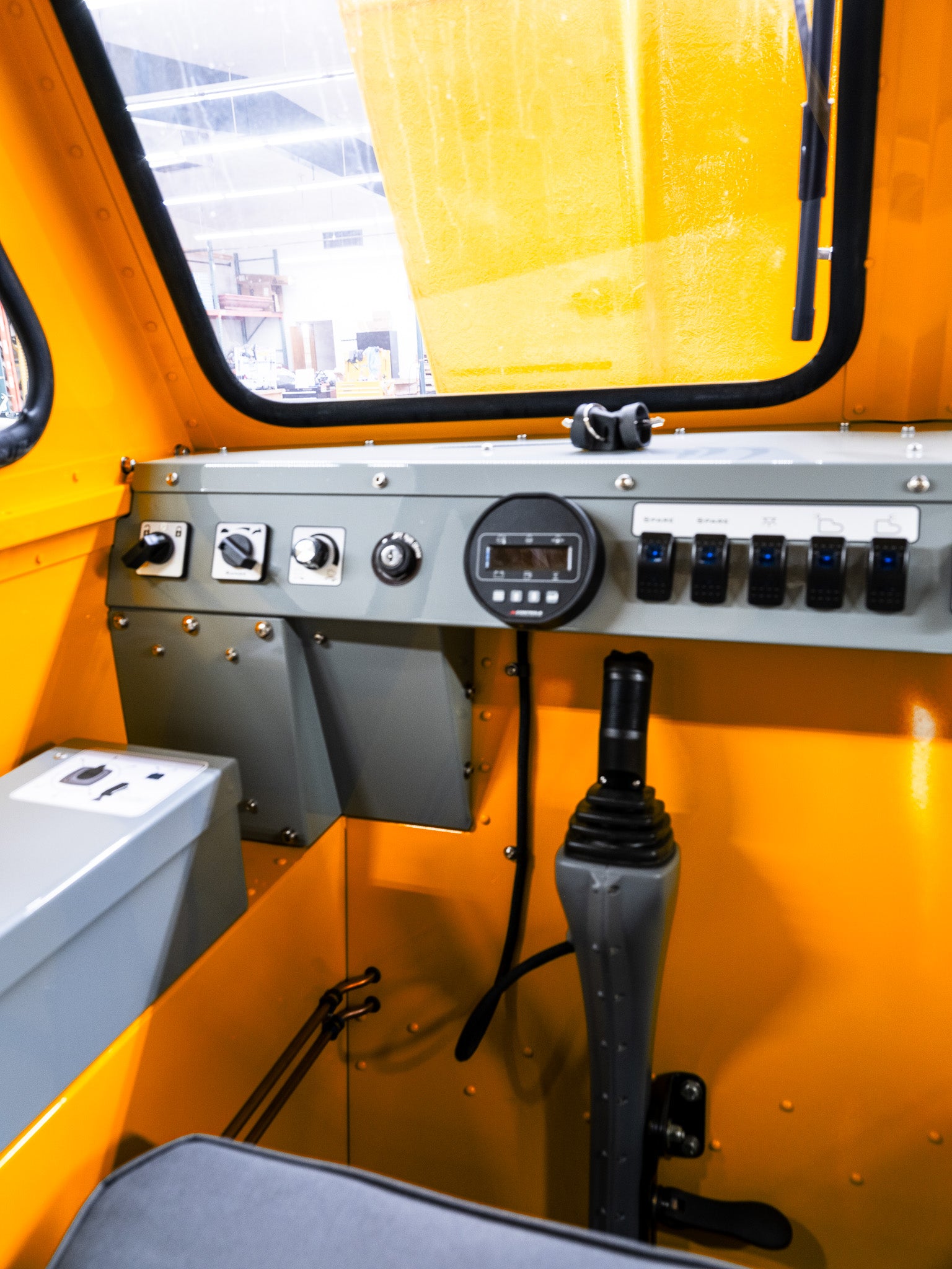Control panel with various switches and a joystick inside a yellow Sno Trac vehicle cabin.